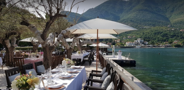 This is a picture of a dining tables in an olive grove near the sea and mountains